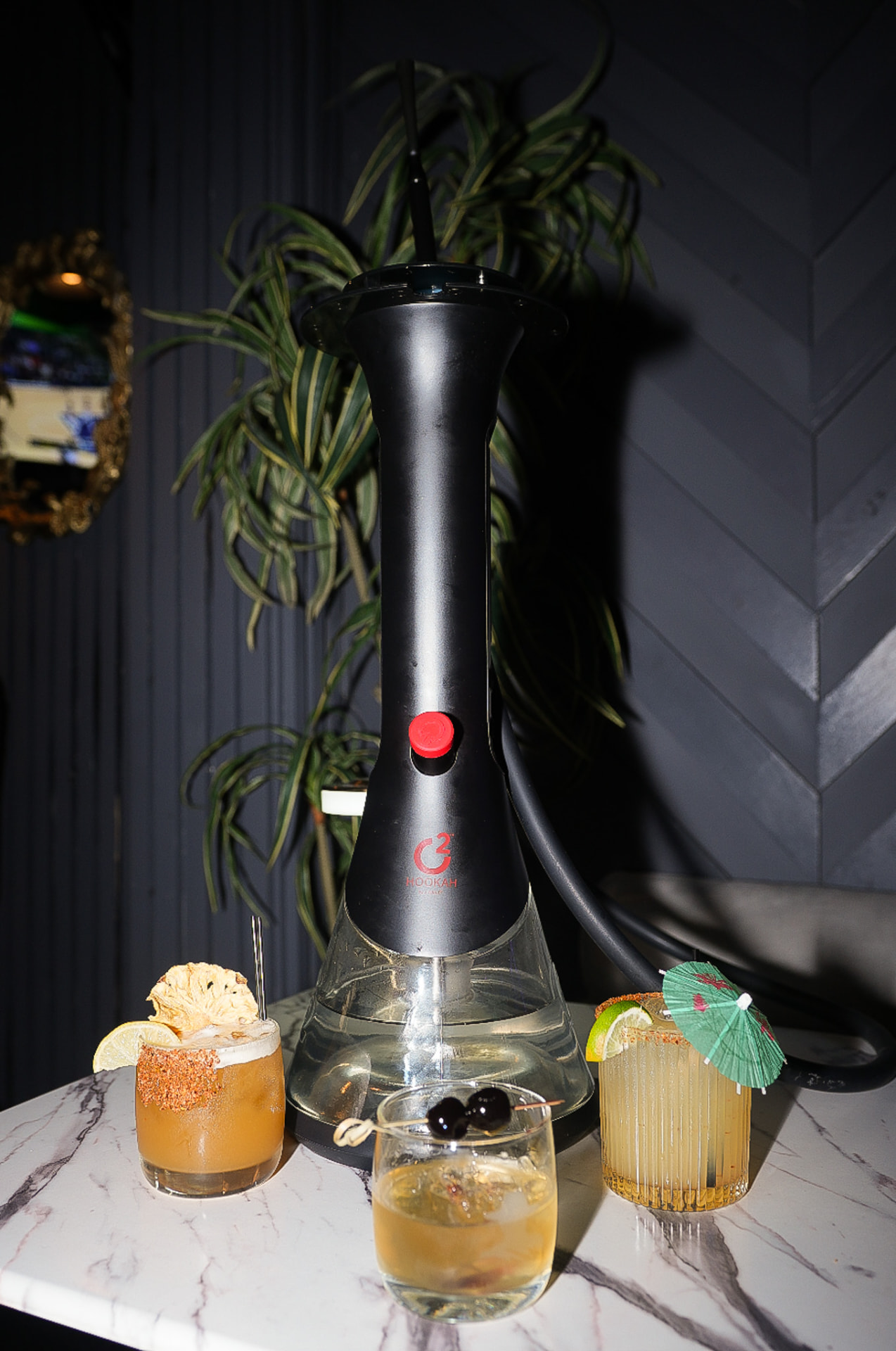 Hookah surrounded by garnished cocktails on a marble table at District385