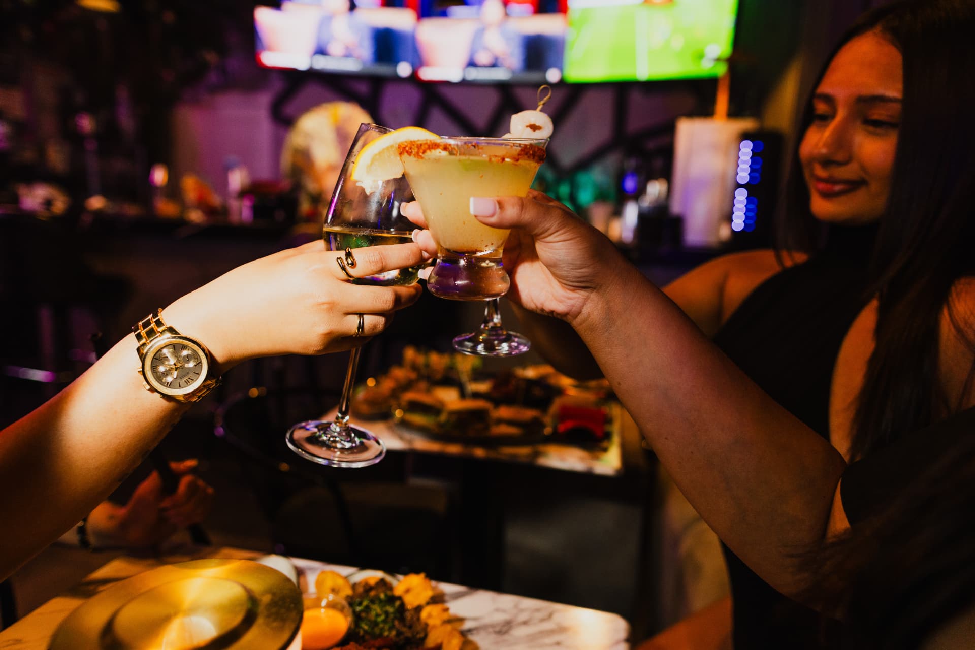 Two guests toasting cocktails over a tapas board at District385