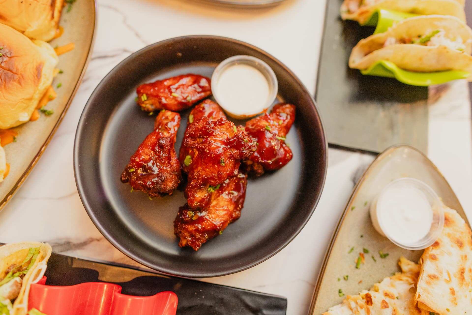 Glazed BBQ chicken wings with ranch, sliders and tacos on a marble table at District385