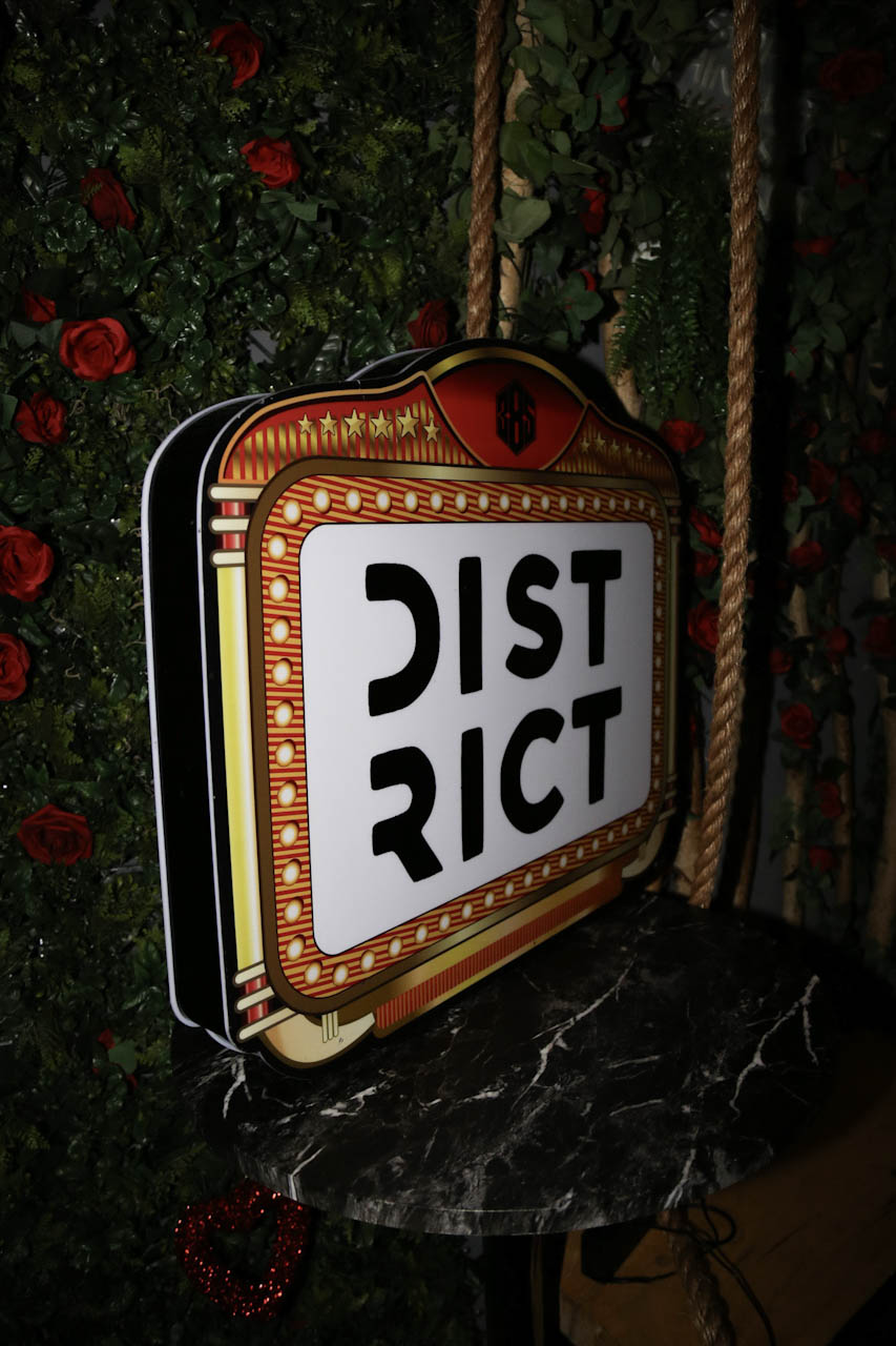 The illuminated DISTRICT marquee sign against the flower wall